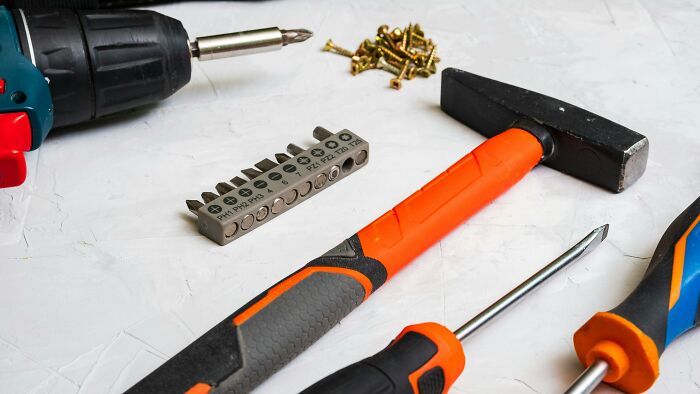 Power drill, hammer, screwdrivers, and screws on a white surface illustrating uncommon hacks for women living alone.