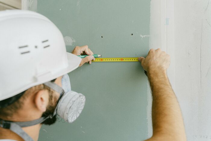 Person wearing a hard hat and mask measuring a wall with a tape measure during an abandoned explorers urban escapade.