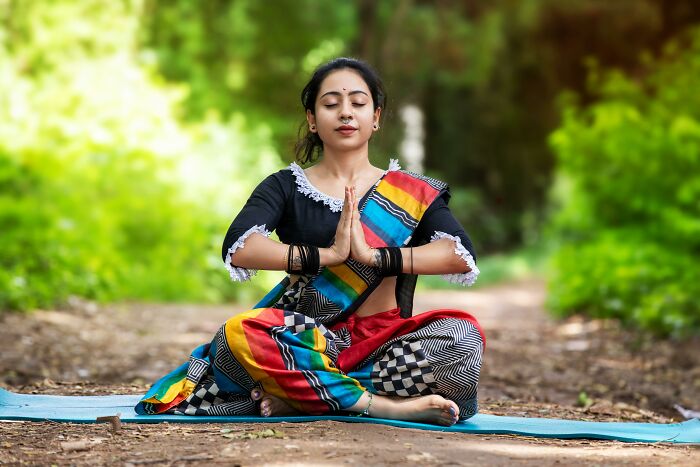 Woman in colorful traditional attire practicing yoga outdoors, reflecting on dark truths of human behavior.