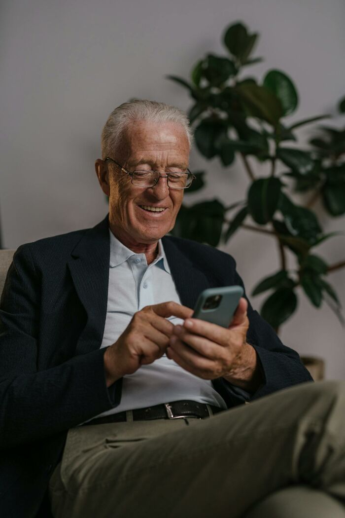 Older man in glasses smiling while using phone, reflecting on insane things male coworkers told women at work.