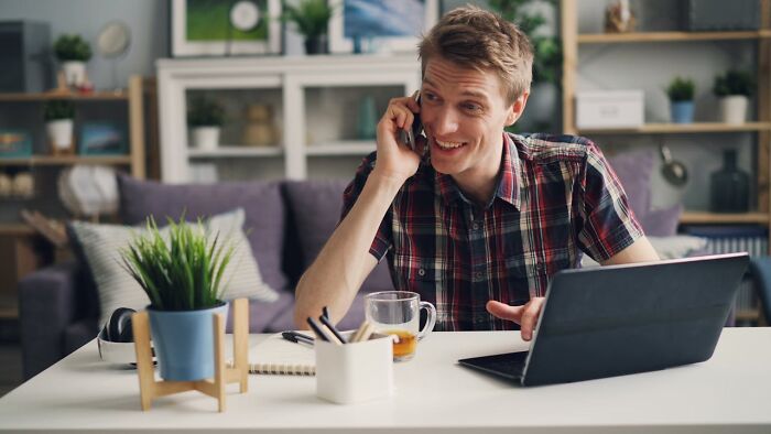 Young man talking on phone while using laptop at home, focusing on moments of really good or really bad genes.