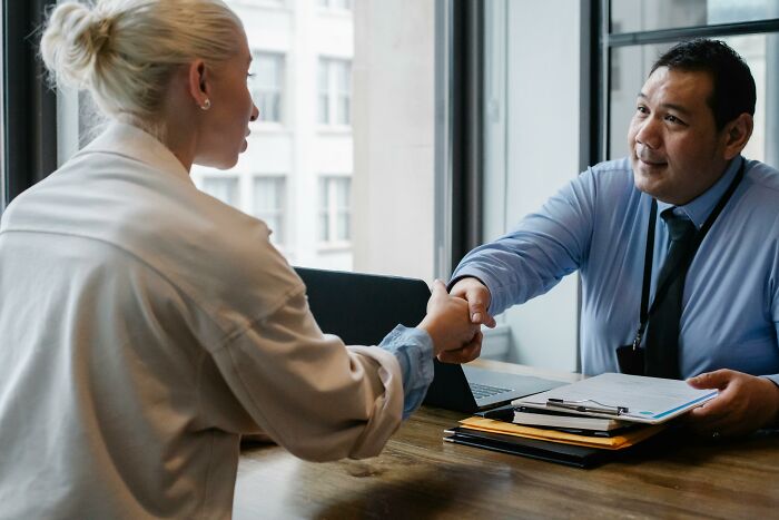 Two colleagues making a tiny gesture by shaking hands warmly, instantly charming each other in a professional setting.