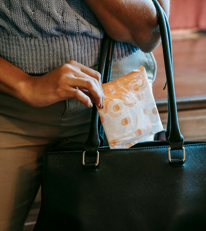 Woman placing a sanitary pad into a black handbag, illustrating postpartum OCD concerns and related experiences.