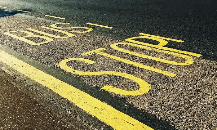 Yellow bus stop sign painted on asphalt road near a sidewalk, highlighting real world privilege and awareness.