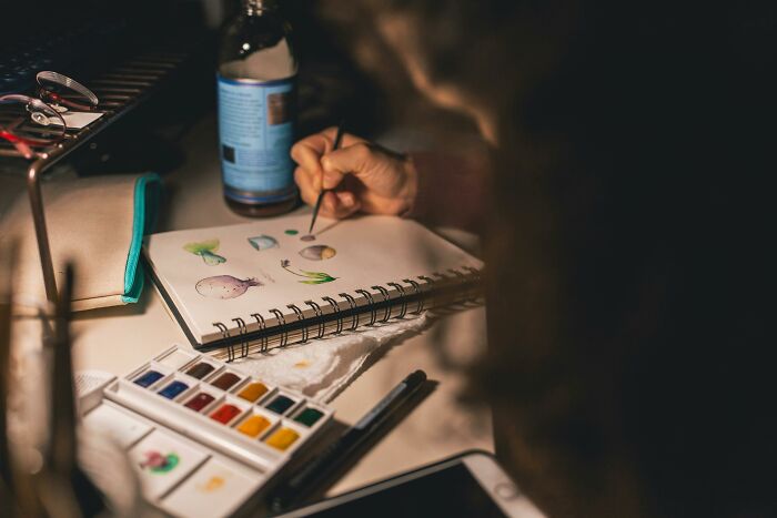 Person painting delicate watercolor designs in a notebook, illustrating subtle signs of low self-esteem in a calm setting.