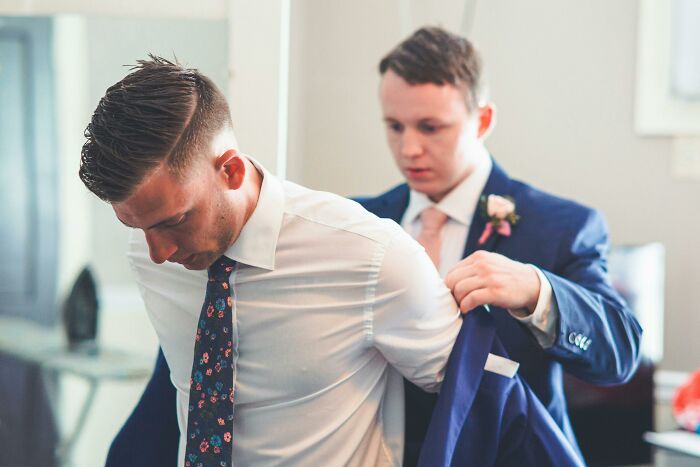 Two men preparing formal attire indoors, illustrating dark truths about human behavior and uncomfortable social interactions.
