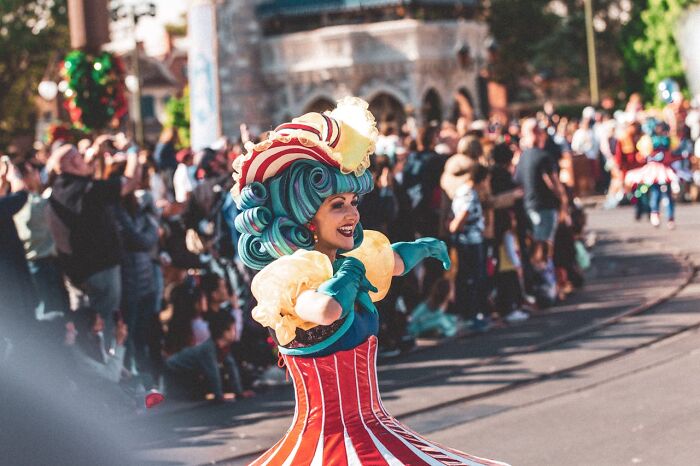 Performer in colorful costume entertains crowd on street with tourists reacting, highlighting travel destinations to avoid.