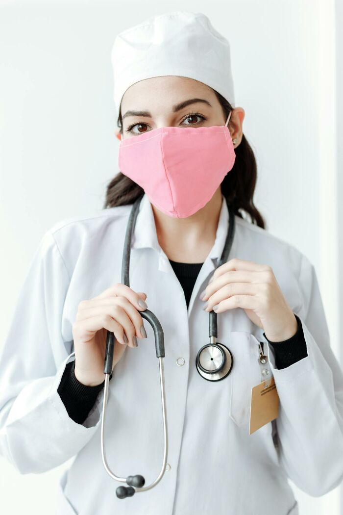 Young private resort worker wearing a white uniform and pink mask holding a stethoscope in a bright setting