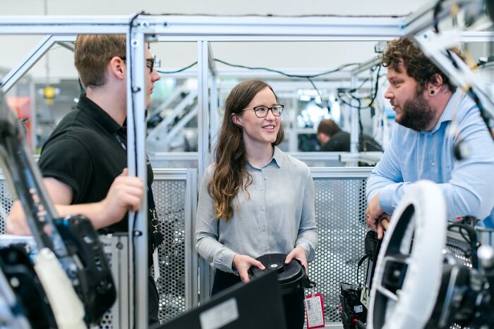 Three coworkers having a casual conversation in an industrial workspace featuring male coworkers and a female employee.