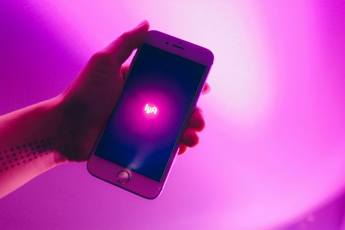 Hand holding smartphone with Lyft app open against a vibrant pink background, representing uncommon hacks for women living alone.