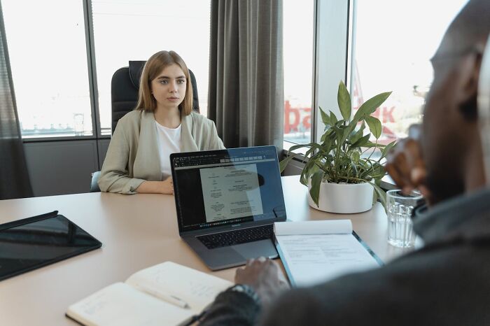 Young woman sitting at office desk during a meeting with male coworker, highlighting workplace interactions and dynamics.