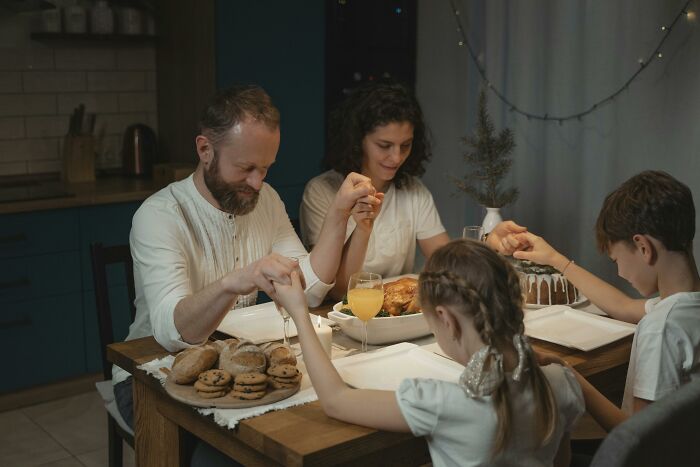 Family holding hands around dinner table in a cozy home.