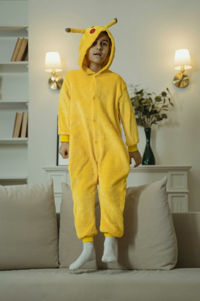 Child wearing a yellow Pikachu onesie jumping on a couch, capturing a fun I was there when it was written moment.