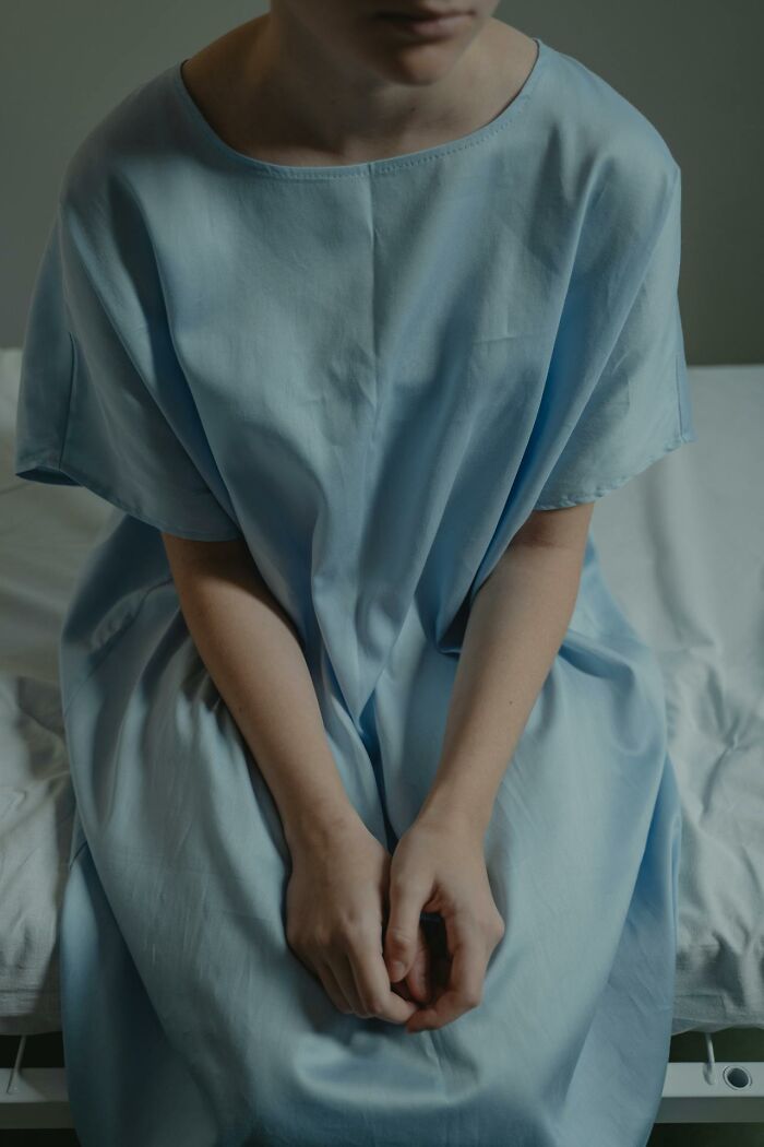 Person sitting on hospital bed wearing a light blue gown, capturing an intense hospital experience moment.