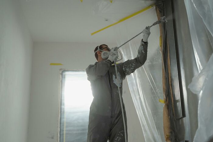 Man in protective gear spray painting a wall, illustrating hidden costs of buying a home like unexpected repairs and renovations.
