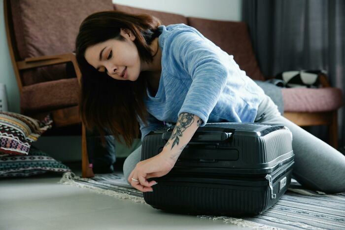 Woman packing a suitcase at home, preparing for travel to avoid being held up in security line before boarding.