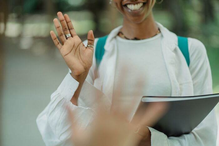 Smiling person waving hand while holding a folder, illustrating casual and harmless looking habits.