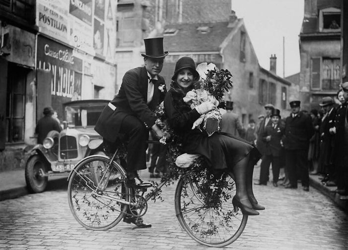 Pareja vestida de época en bicicleta adornada, mostrando un lado distinto de la historia en foto interesante y antigua.