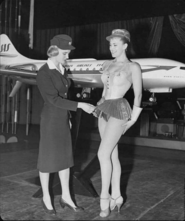 Vintage photo showing a flight attendant and a woman in costume with a model airplane in the background.