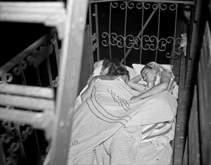 Black and white photo showing two people sleeping on a balcony, capturing a timeless glimpse of the past.