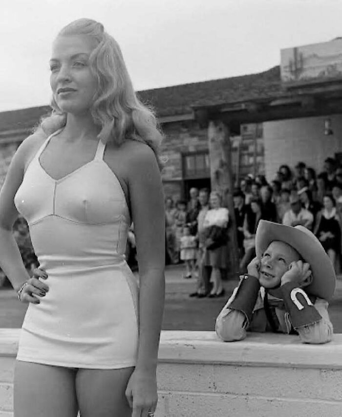 Vintage black and white photo of a woman in a swimsuit and a boy dressed as a cowboy, capturing timeless moments from the past.