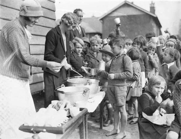 Niños en fila recibiendo comida en una distribución histórica, mostrando un lado distinto de la historia en una foto antigua.