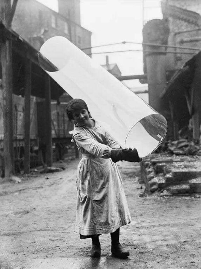 Joven trabajadora sosteniendo un tubo de vidrio gigante en fábrica, mostrando un lado distinto de la historia industrial.