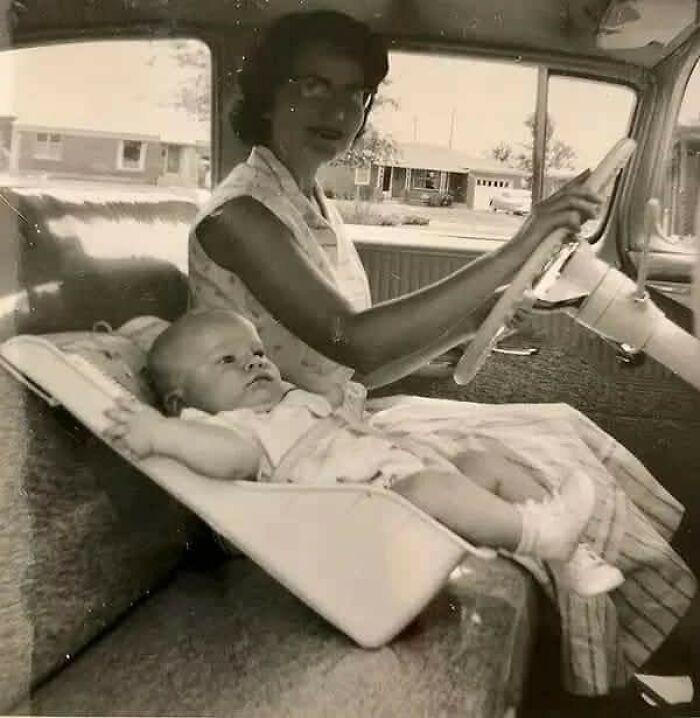 Vintage photo showing a woman driving a car with a baby lying on a reclining seat, capturing timeless moments from the past.