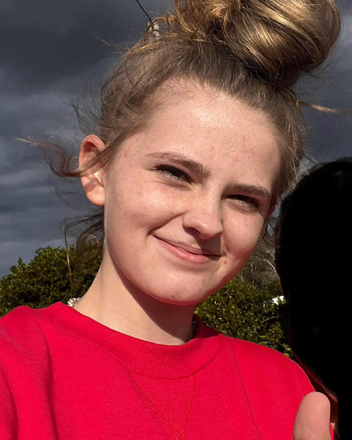Teen mourner with hair in a bun expressing emotion outdoors during Phoebe Bishop funeral service.