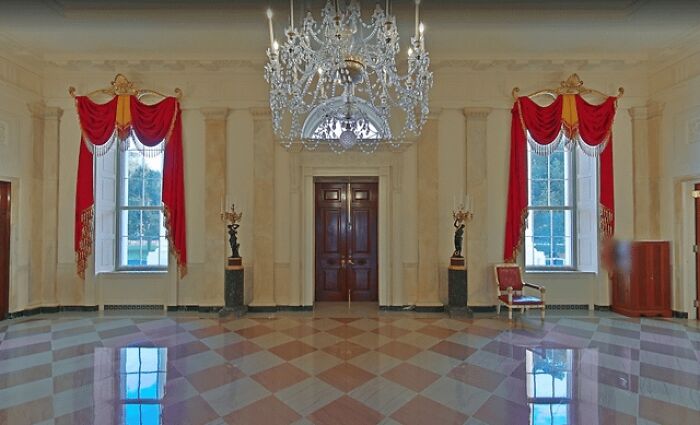 Spacious room with polished checkered floor, ornate chandelier, and red draped curtains showcasing alternative angles unseen.
