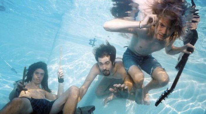 Three young men underwater holding musical instruments, showcasing photos alternative angles unseen in creative setting.