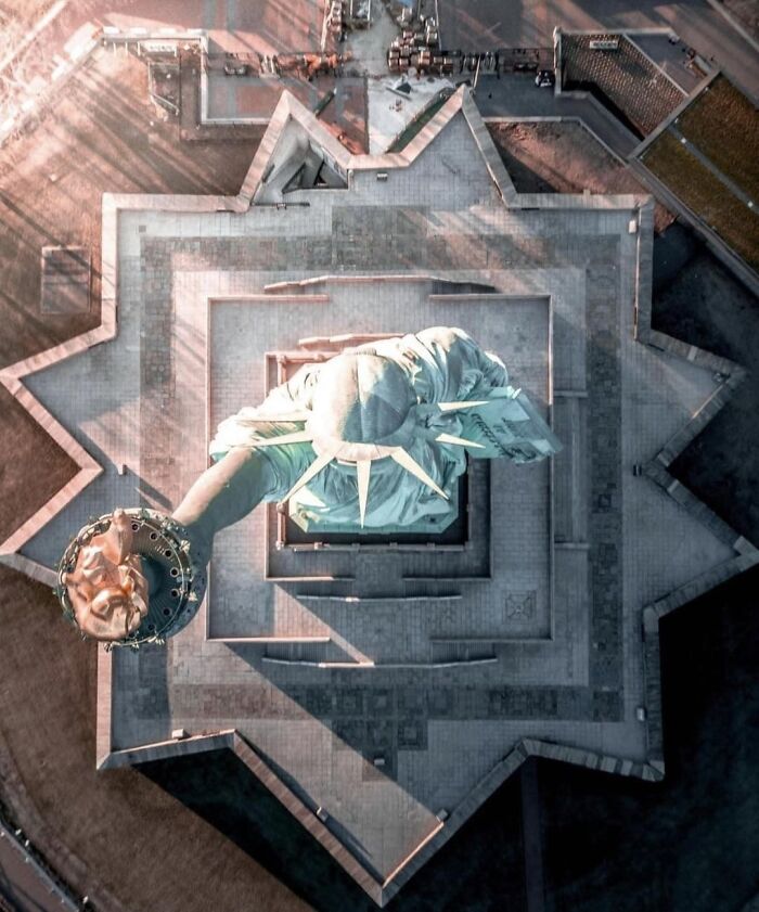 Aerial drone photo showing unseen alternative angles of the Statue of Liberty torch and crown area at sunrise.