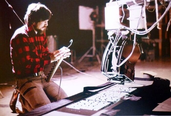 Technician in a red plaid shirt adjusting a robotic arm with alternative angles of photos in a dimly lit studio setting.