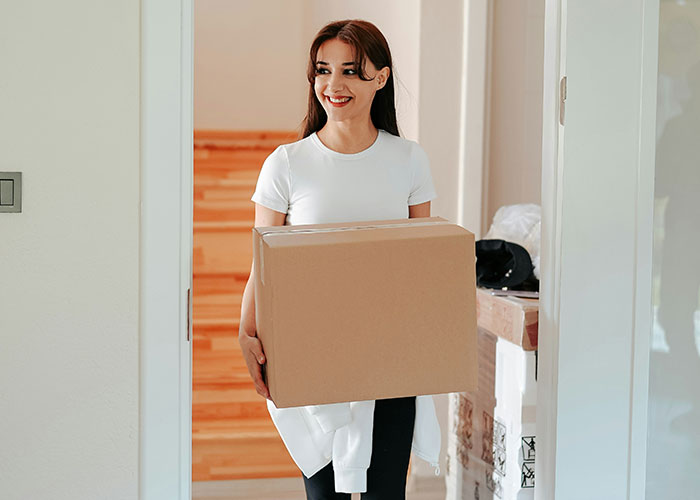 Smiling woman carrying a large cardboard box indoors, symbolizing a dad desperate to restore peace at home. Smiling woman carrying a large cardboard box indoors, symbolizing a dad desperate to restore peace at home.