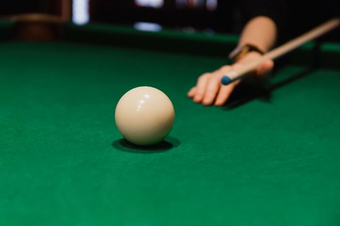 Close-up of a person aiming a cue stick at a cue ball on a green pool table, highlighting unexpected airport security issues.