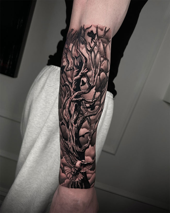 Forearm poison tree tattoo with detailed branches, dark shading, and a bird in flight against a cloudy background. Forearm poison tree tattoo with detailed branches, dark shading, and a bird in flight against a cloudy background.