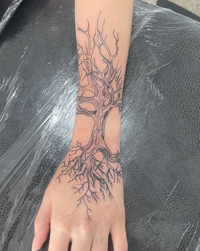 Black ink poison tree tattoo with intricate branches and roots covering the wrist and hand, showcasing detailed style and placement. Black ink poison tree tattoo with intricate branches and roots covering the wrist and hand, showcasing detailed style and placement.