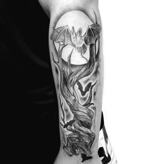 Black and grey poison tree tattoo on forearm featuring twisted branches, flying bats, and a full moon background. Black and grey poison tree tattoo on forearm featuring twisted branches, flying bats, and a full moon background.