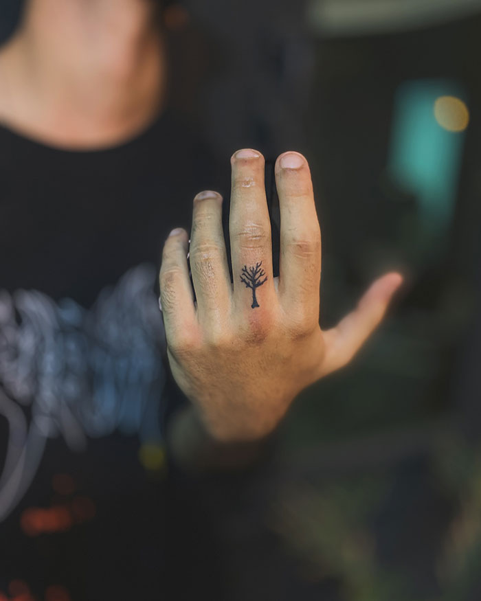 Close-up of a hand with a small poison tree tattoo on the finger, showcasing tattoo styles and placement ideas. Close-up of a hand with a small poison tree tattoo on the finger, showcasing tattoo styles and placement ideas.