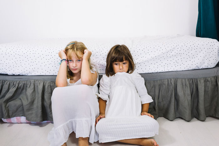 Two young girls in white dresses sitting on the floor, reflecting concerns about kids safety around pool fences.