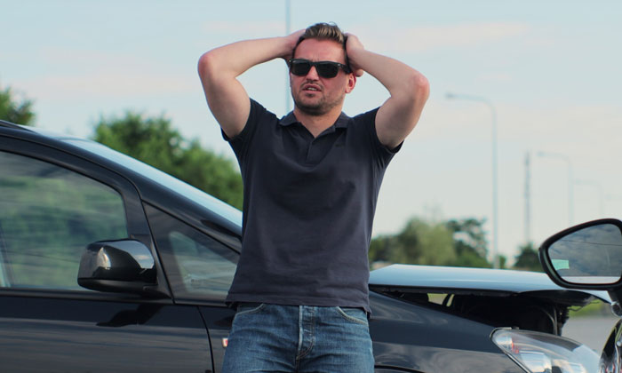 Man wearing sunglasses and a black shirt stands frustrated next to his Porsche parked across three handicap spots.