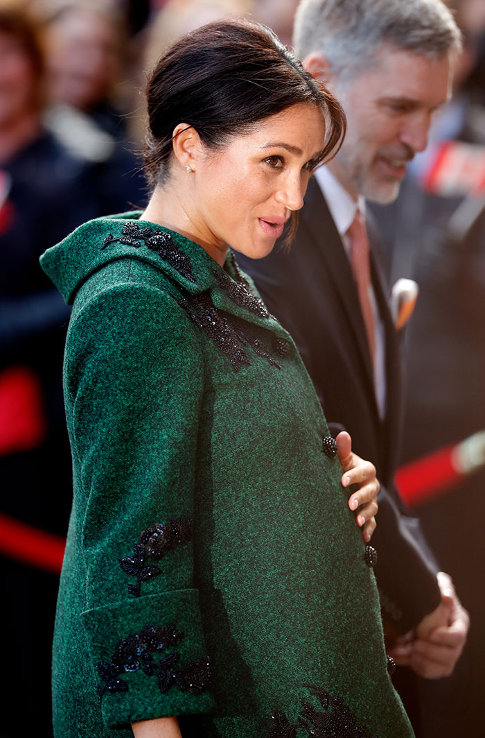 Meghan Markle wearing a green coat, holding her baby bump, amid renewed twerking pregnancy video conspiracy theory.