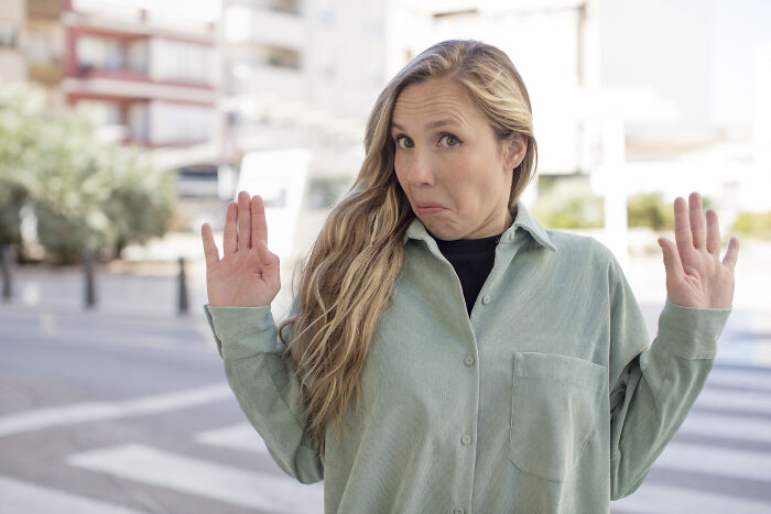 Young woman outdoors with raised hands and unsure expression.