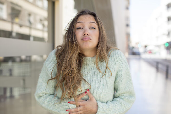 Young woman in a green sweater outdoors holding her stomach, illustrating pregnancy and childbirth facts.
