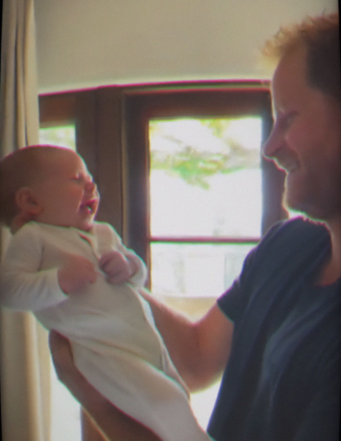 Man holding smiling baby indoors near window, related to Meghan Markle Father's Day post criticized for paid child actors and rented kids. Man holding smiling baby indoors near window, related to Meghan Markle Father's Day post criticized for paid child actors and rented kids.