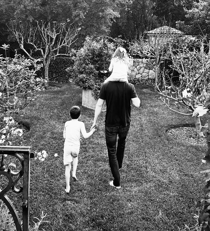 Man walking in garden holding hands with two children, related to Meghan Markle Father's Day post controversy. Man walking in garden holding hands with two children, related to Meghan Markle Father's Day post controversy.