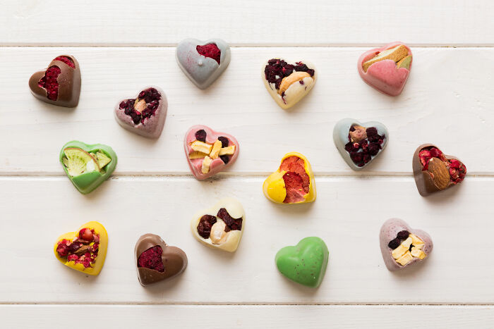 Assorted colorful heart-shaped chocolates with nuts and dried fruit on a white wooden surface, representing rich kid treats.