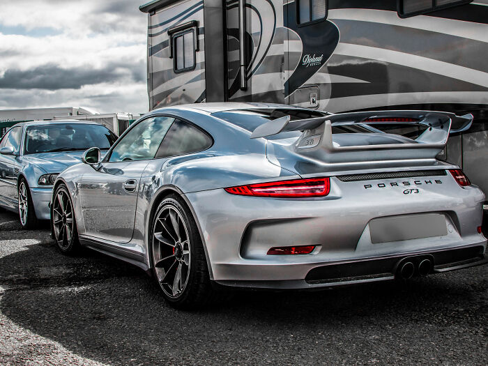 Silver Porsche GT3 parked near luxury RV, illustrating rich kid lifestyle and meltdowns at private schools.