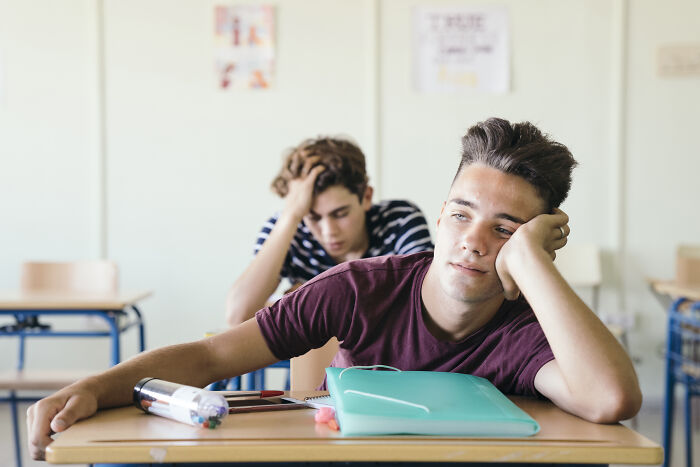 Teen boy showing a meltdown in a private school classroom, sitting bored with head resting on hand.