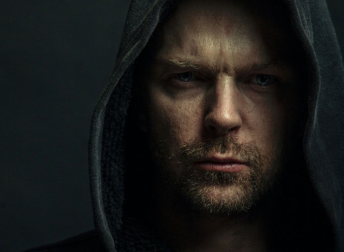 Close-up of a man with intense eyes wearing a dark hood, illustrating psychologists' experiences with patients who scared them.